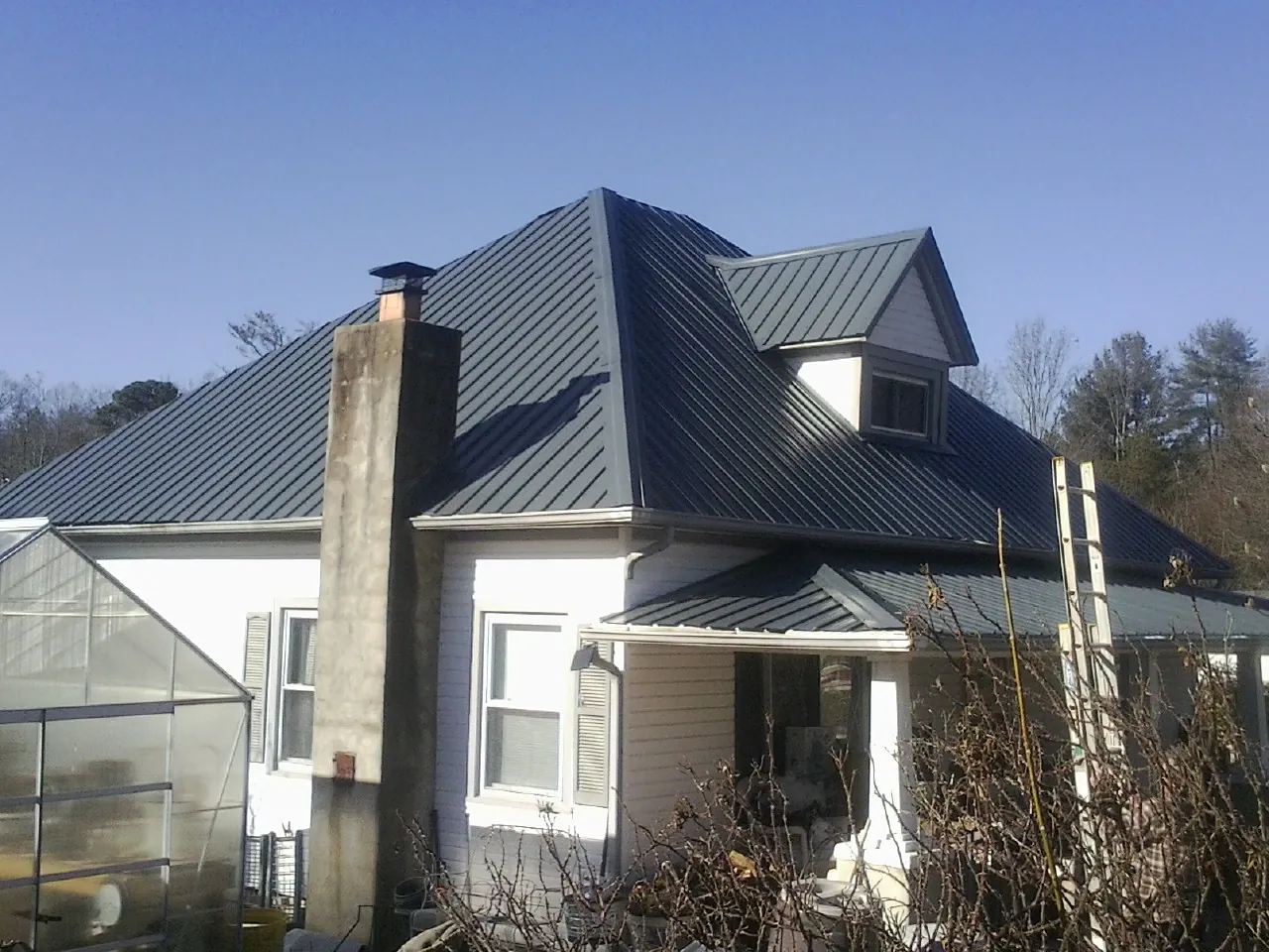 Dark blue standing seam metal roof on a white farmhouse with dormer — Slate & Tile Roof Repair by Roofing Brothers in Flat Rock