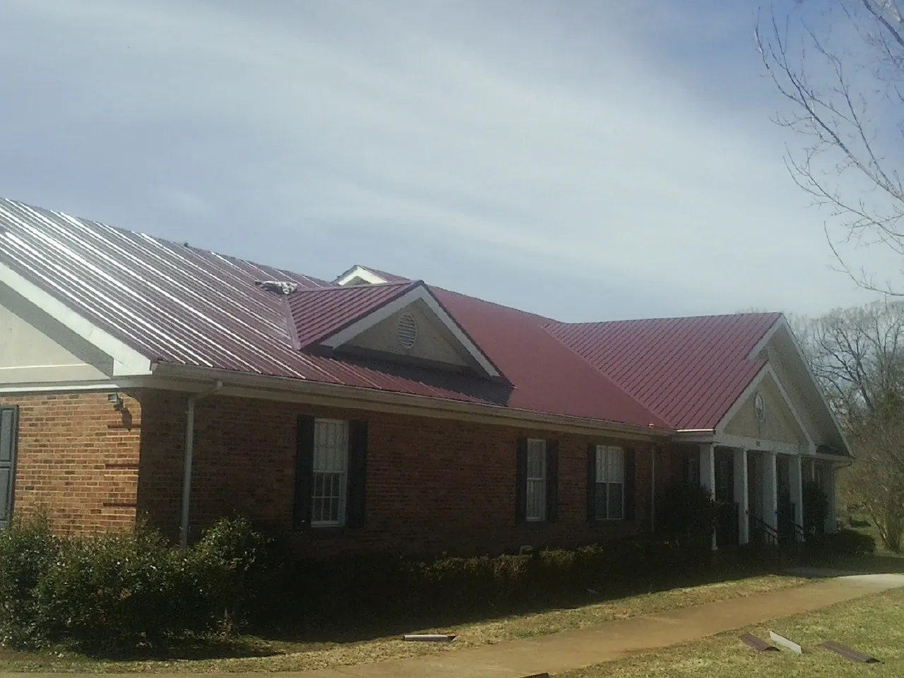 Red metal roof with gabled entries on a long brick building, from a Hail Damage Roof Repair job in Flat Rock