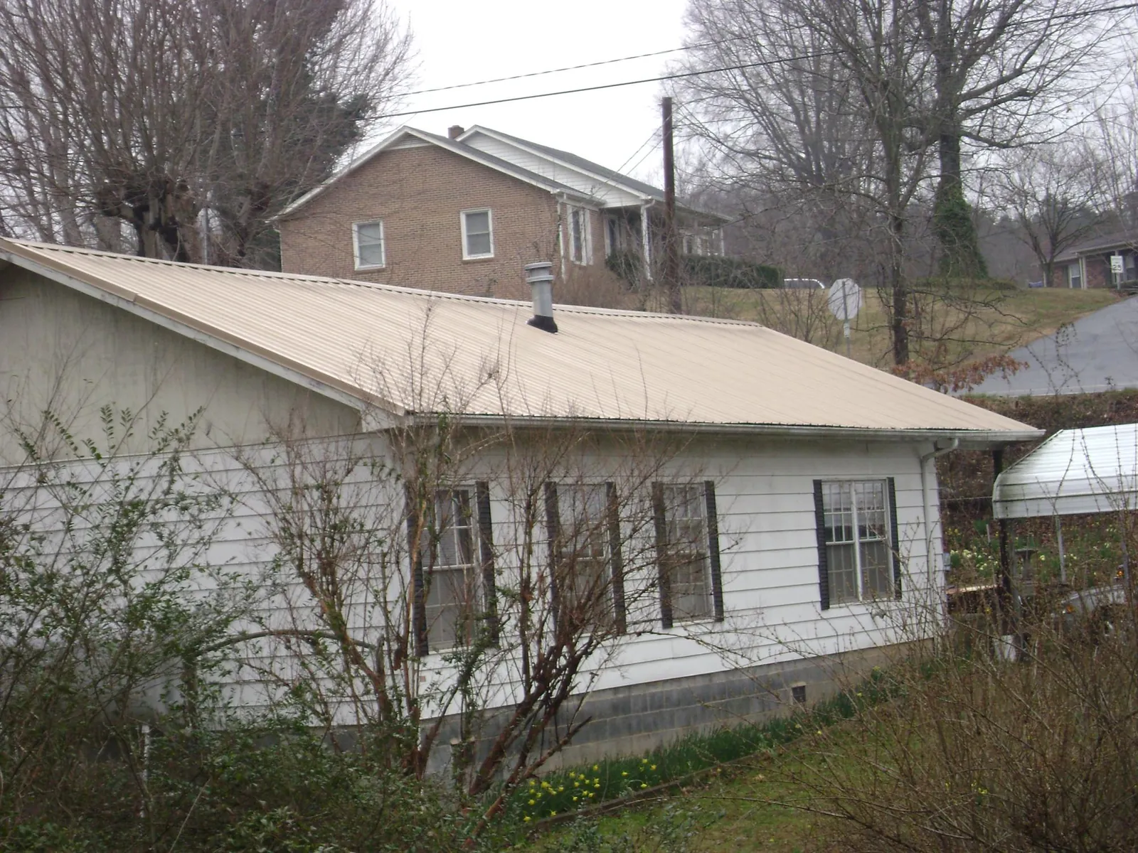 Tan metal roof on a white sided house set into a hillside — Commercial Roofing by Roofing Brothers in Flat Rock